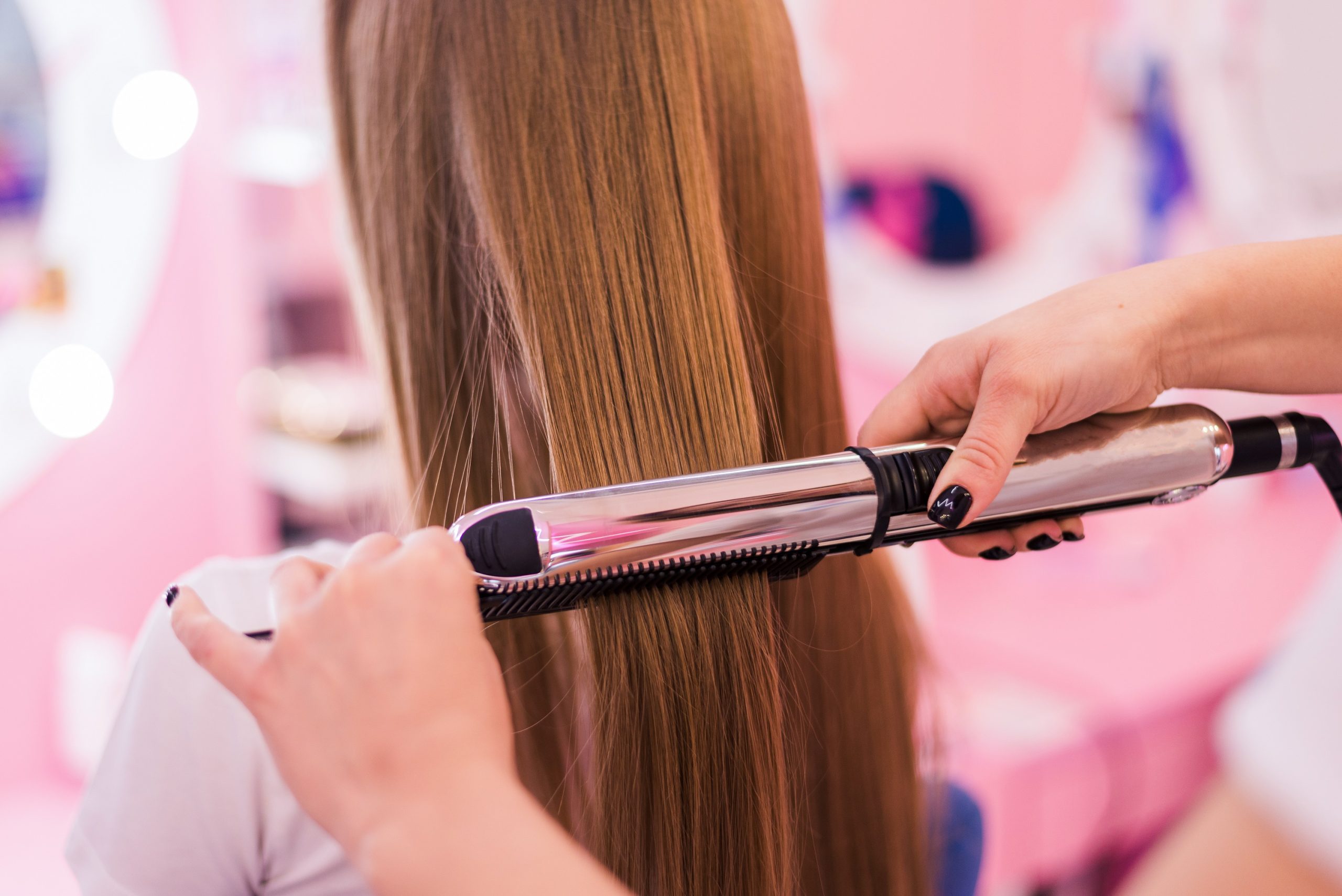 young woman getting her hair curled by stylist at parlor. Beautiful young hairdresser giving new haircut to female